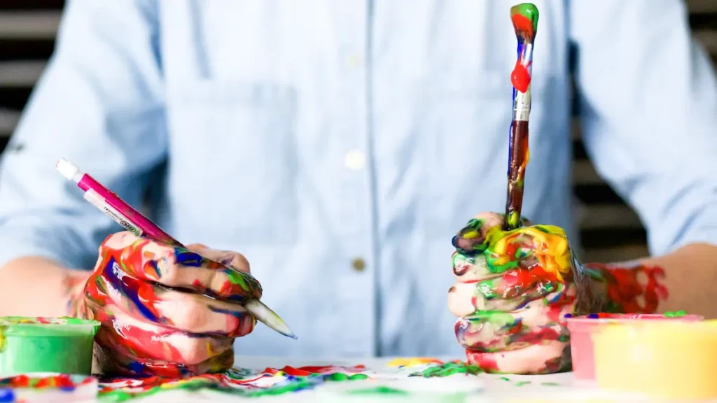 Painter with hands full of paint holding brushes in each hand