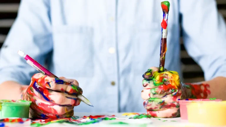 Painter with hands full of paint holding brushes in each hand